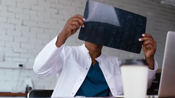 African American Black Man Doctor Looking at MRI Brain Scan Image While Working at Desk with Laptop