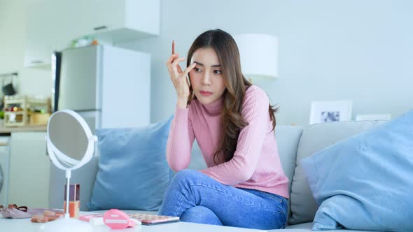 Asian frustrated attractive women look at mirror and make up herself in hurry in living room at home