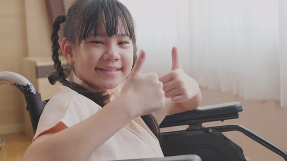 Portrait of Asian little illness girl sit on wheelchair and thumbs up with cheerful in hospital.