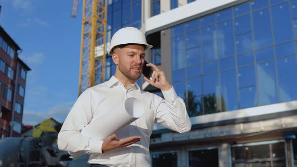 Evil Engineer in a White Shirt and Helmet Works on the Construction of a Modern Glass Building