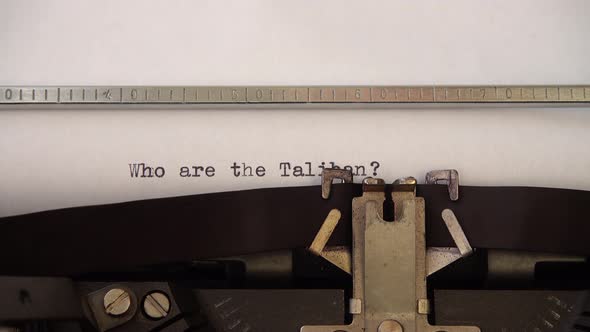 Typing phrase Who are the Taliban ? on retro typewriter. Close up.