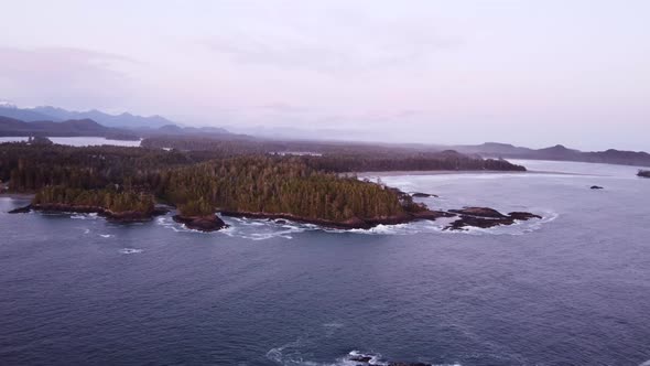 A panning drone video over the ocean next to a forested coast during sunset with mountains visible i