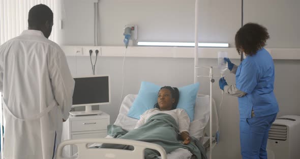 Doctor with Clipboard Examining Sick African Woman in Hospital Bed While Nurse Checking Iv Dripper