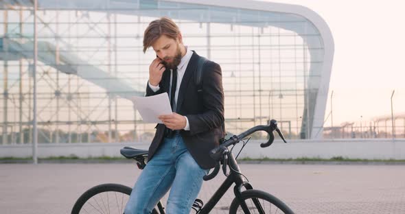 Man Which Standing Near His Bike on the Office Building and Has Phone Conversation