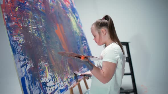 Girl with Special Needs Draws with a Brush on a Large Canvas in a White Room Kid Girl with Down