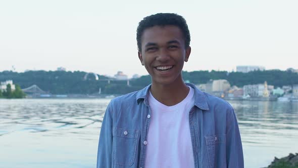 Black Teen Boy Laughing Sincerely Standing Against Cityscape, Enjoying Life