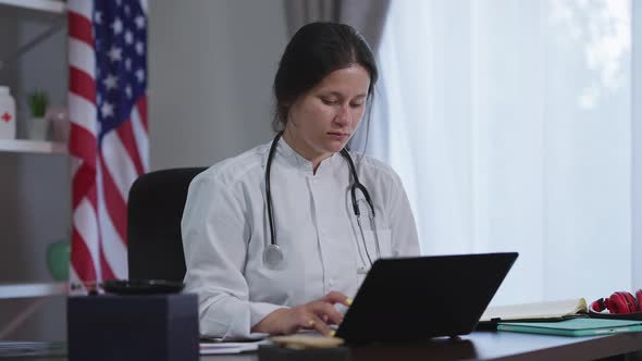 Portrait of Concentrated Young Caucasian Female Doctor Typing on Laptop Keyboard Searching