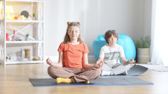 Wide Shot Portrait of Cute Caucasian Girl and Boy Sitting on Exercise Mat in Lotus Pose