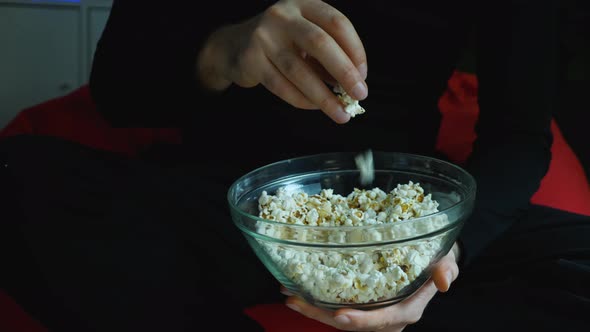 Close-up of a man's hand taking large handfuls of popcorn from a glass cup