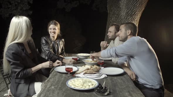 Group of Four Happy Men and Women Friends Smile and Enjoy Aperitif in Outdoor Rural Scenic at Night