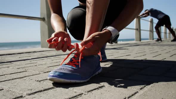 Fit woman tying shoelaces on a promenade at beach 4k