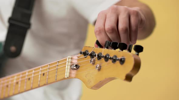 Cropped Photo of Young Male Guitarist in Casual Clothing Fixing Tuning Pegs on Electric Guitar