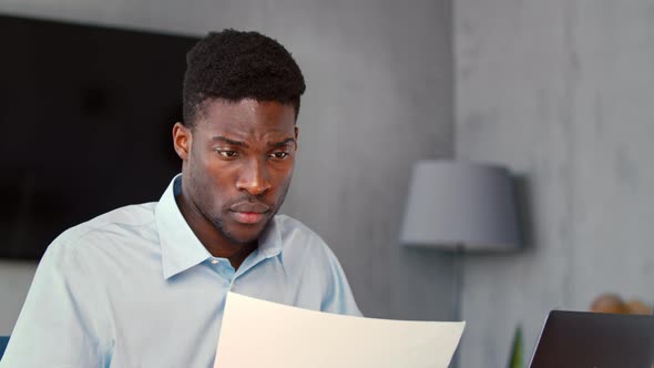 Young businessman in shirt checking analytics on paper and on computer