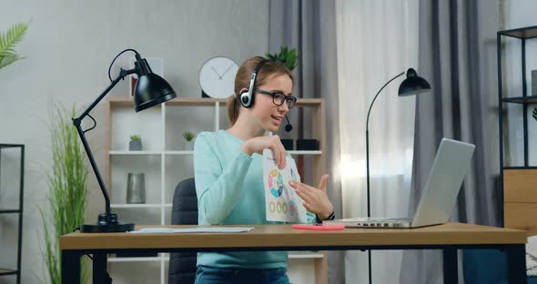 Female Student in Headphones Presenting Her Report with Infographics to Teacher Online Seminar