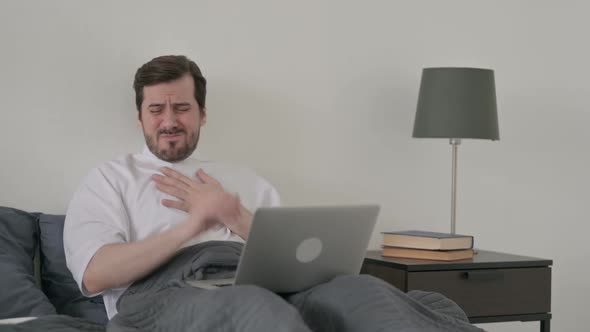 Young Man Coughing While Working on Laptop in Bed