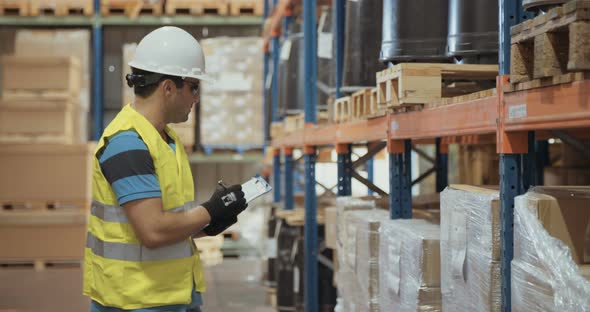 Logistics worker wearing a helmet working in a large warehouse checking inventory