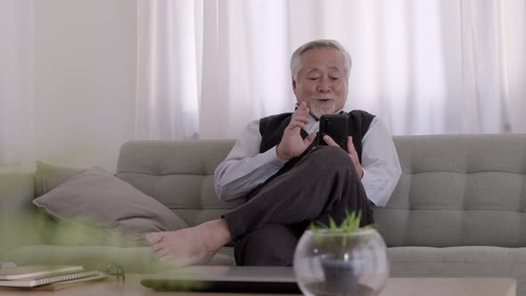 An Asian Elderly video call with smartphone on the sofa on a relaxing day.