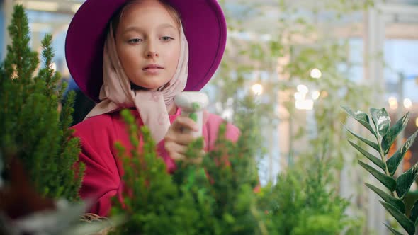 Young Florist Woman in Pink Hat Spraying Plants in Indoor Garden