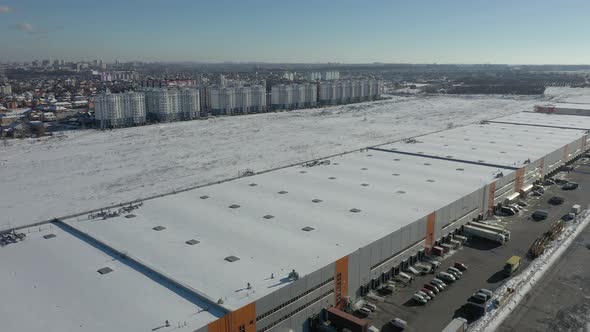 Trucks stand near a large warehouse loading cargo. Shooting from the air