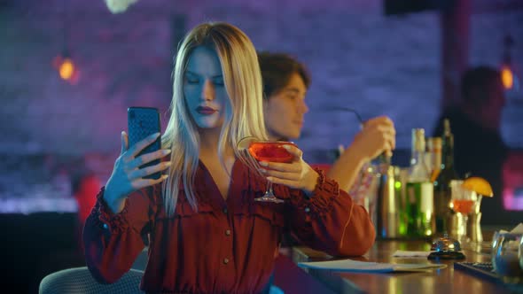 Young Woman Sitting By the Bartender Stand and Using Her Phone - Taking a Selfie with a Drink