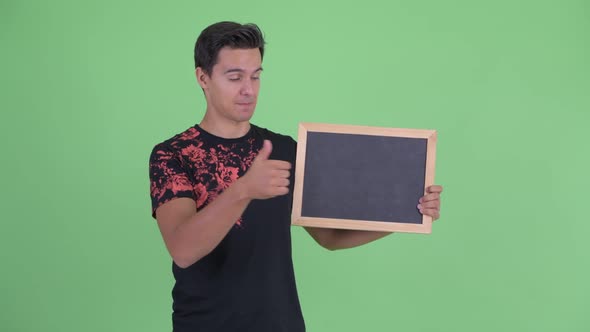 Happy Young Handsome Man Holding Blackboard and Giving Thumbs Up