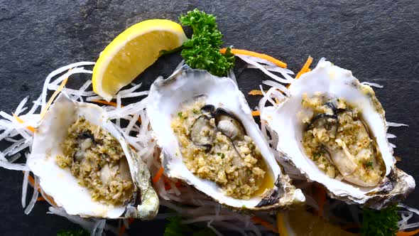 Cooked Oysters in Shells with Lemon and Garlic on Black Textured Slate Top View