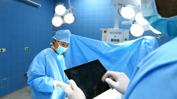 Surgeon using digital tablet while coworker operating patient in operation room