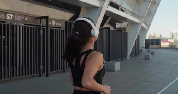 Side View of Athletic Young Woman in Headphones Jogging and Listening Music Outdoors in Slow Motion