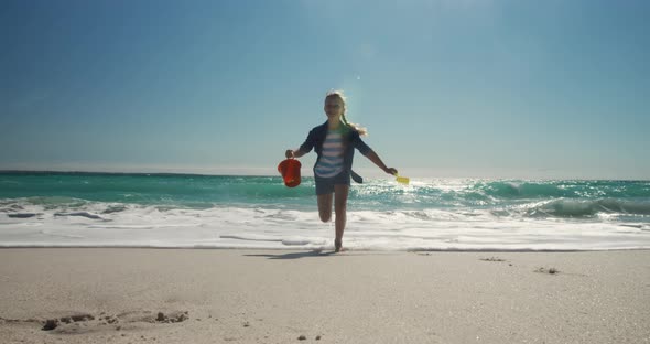 Young girl running at the beach with toys