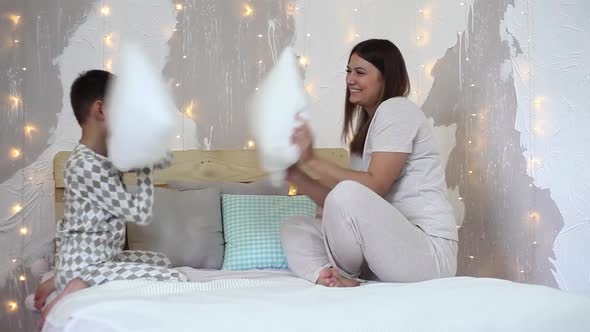 A Girl and a Little Boy Have Fun Hitting Each Other with Paddles Sitting on the Bed