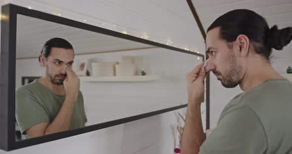 Handsome Man Wiping His Face with a Cotton Sponge Standing in Front of a Mirror