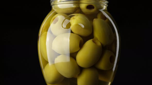 pitted green olives in glass jar on black background