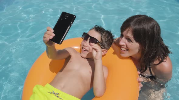 Smiling Mother and Child having fun in Swimming pool, taking photos and Videos, Summer Vacation