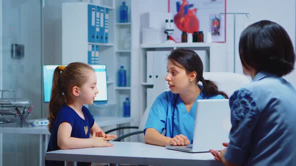 Nurse Talking with Child and Writing on Laptop