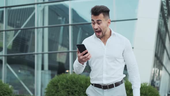 Portrait Of Young Man. Business Style. Guy Looks At The Phone And Starts To Run. He Is In Hurry.