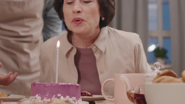 Senior Woman Blowing Out Candle On Birthday Cake