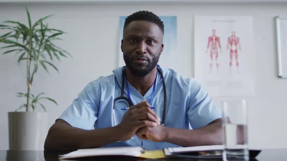 African american male doctor at desk talking and gesturing during video call consultation