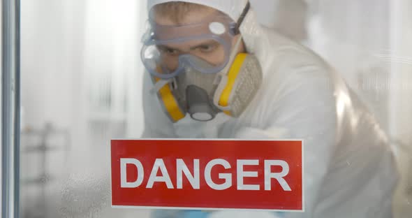 Medical Worker in Ppe Suit and Respiratory Mask Cleaning Glass Door with Detergent and Cloth