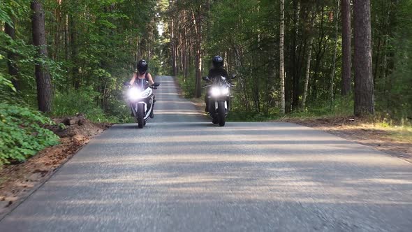 Two Women Riding Motorcycles on an Empty Narrow Road in the Forest in Daylight