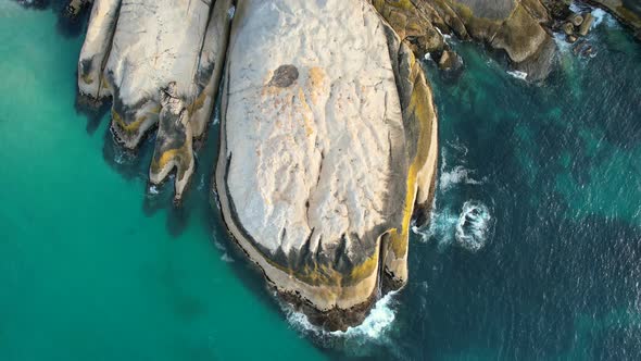 blue ocean waves crashing on large boulders at Llandudno Beach in Cape Town, top down aerial