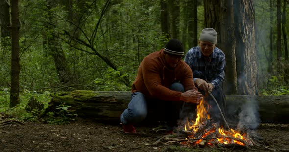 Handsome Guy Warms Hands at Campfire and Sits Near Father