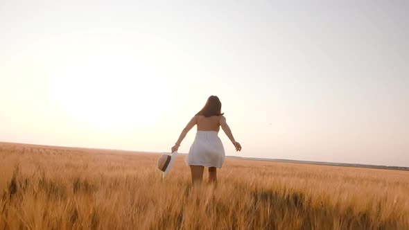 Happy Free Young Woman Runs in Slow Motion Across Field Touching Ears of Wheat with Her Hand