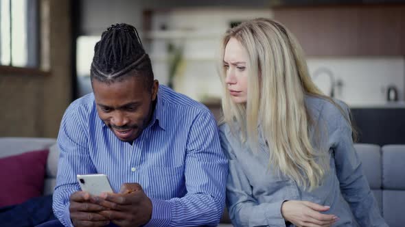 Jealous Caucasian Wife Looking at Smartphone of African American Husband Talking and Gesturing