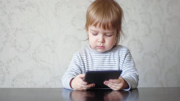 Small Kid Boy Using Digital Tablet Technology Device Sitting at Table