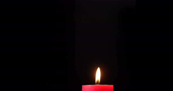 A single red paraffin candle burning. Isolated candlelight on dark background. 