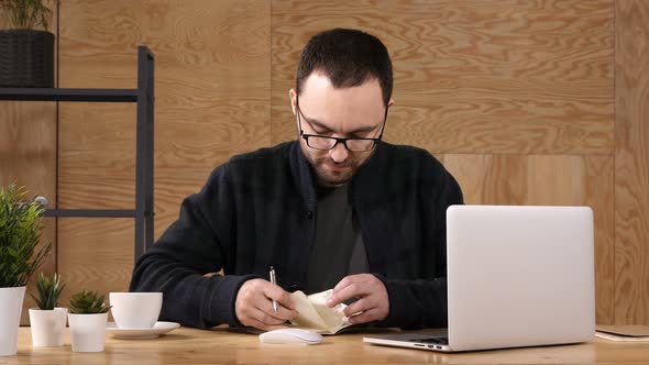 Hipster Taking Notes Down From His New Laptop Computer While Browsing the Internet