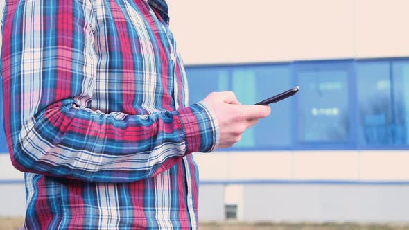 A man's hand in a checkered red-blue shirt holds a smartphone.