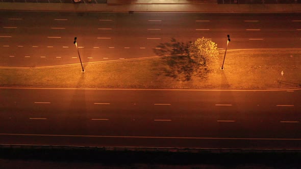 an aerial view of a highway at night with orange hue street lights turned on. The drone camera tilte