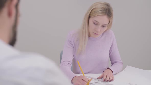 Close-up Portrait of Blond Caucasian Woman Drawing Blueprint, Shaking Customer's Hand and Smiling