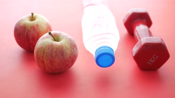 Fresh Drinking Water Apple and a Pink Color Dumbbell on Red